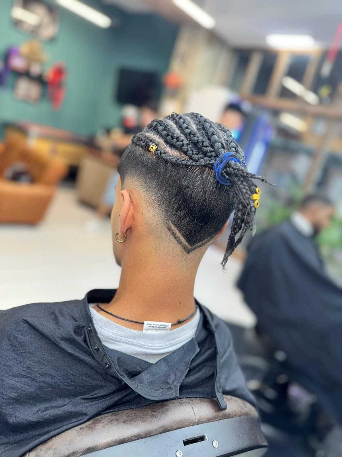 Hombre con cabello trenzado y corte de pelo desvanecido en una barbería.