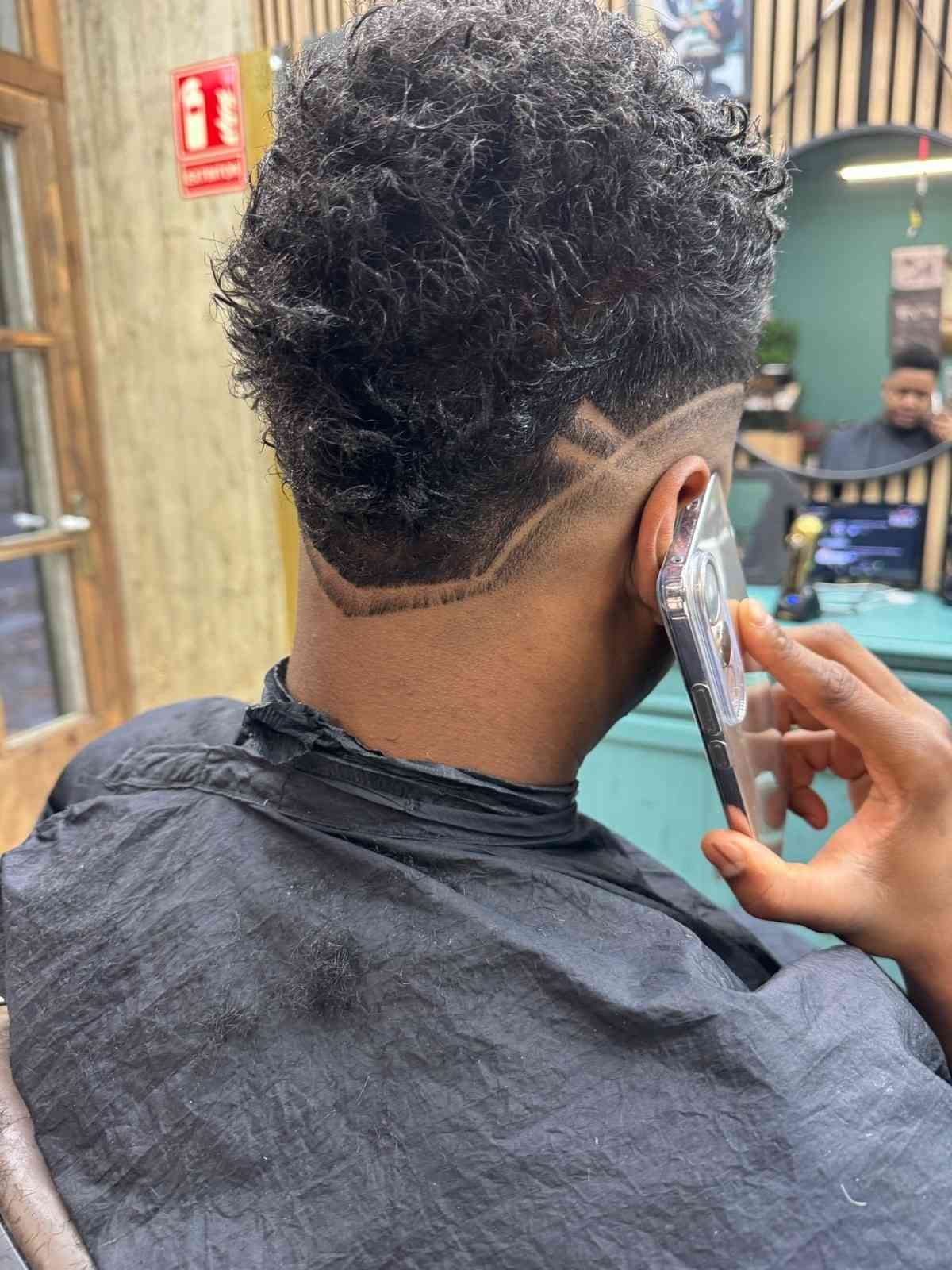 Hombre con un corte de pelo texturizado y un diseño en el costado de la cabeza, hablando por teléfono en una barbería.