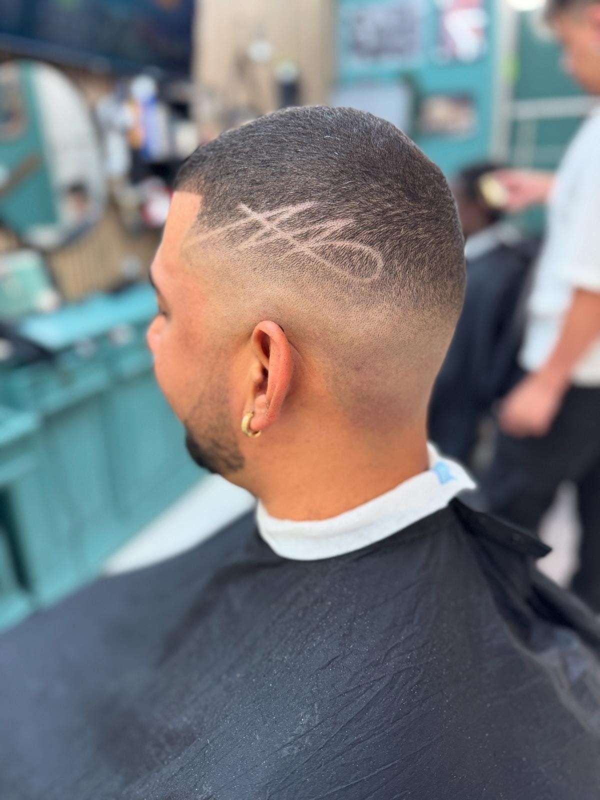Hombre con un corte de pelo descolorido y un diseño en el costado de la cabeza, en una barbería.