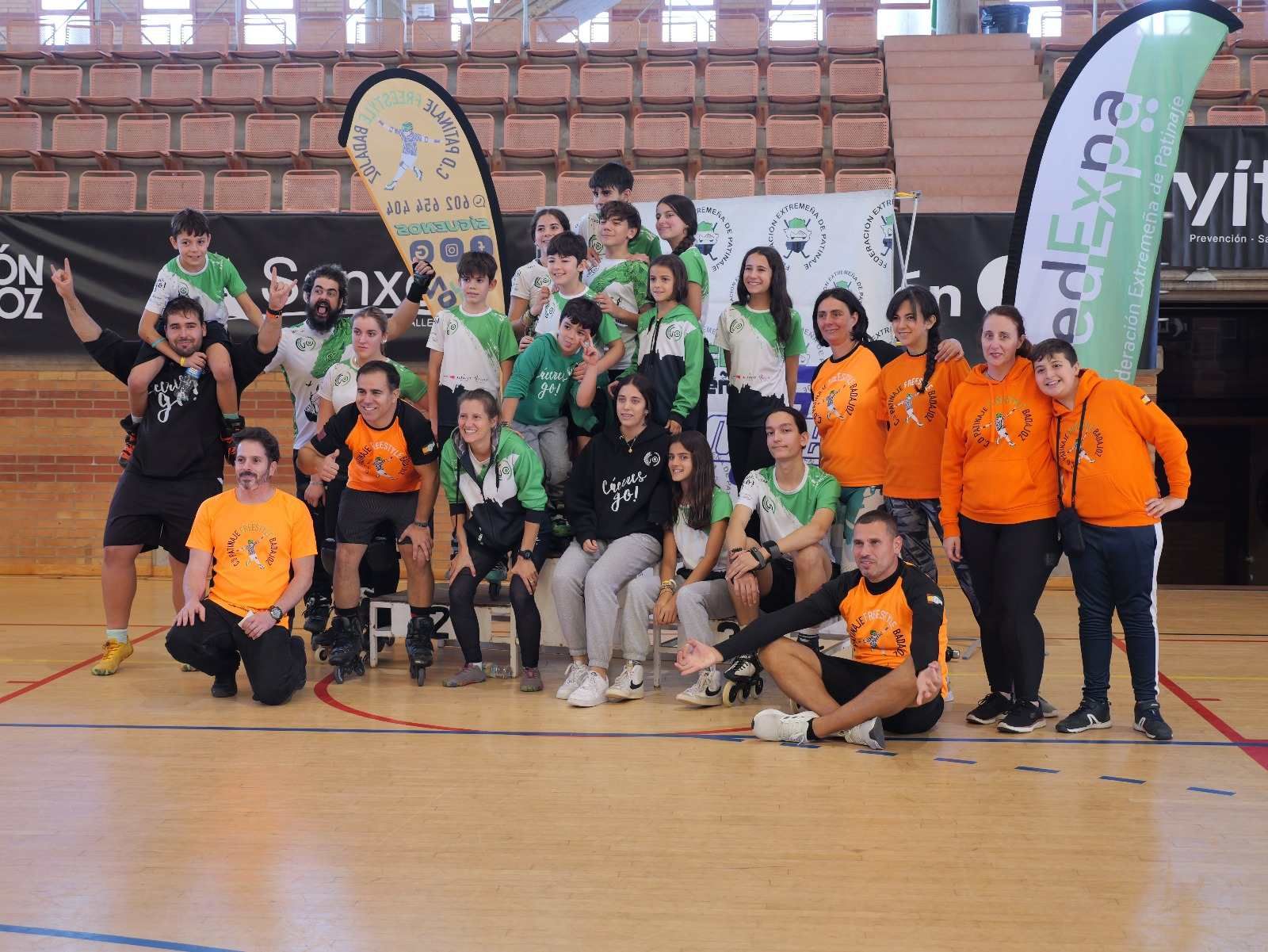 Fotografía grupal de personas en un gimnasio; algunos visten trajes de color naranja, verde y negro; caras sonrientes.