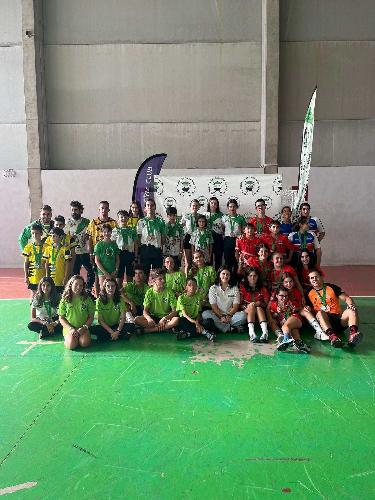 Grupo de jóvenes con uniforme deportivo posando en un espacio cerrado. Uniformes verdes y rojos, en una cancha verde.