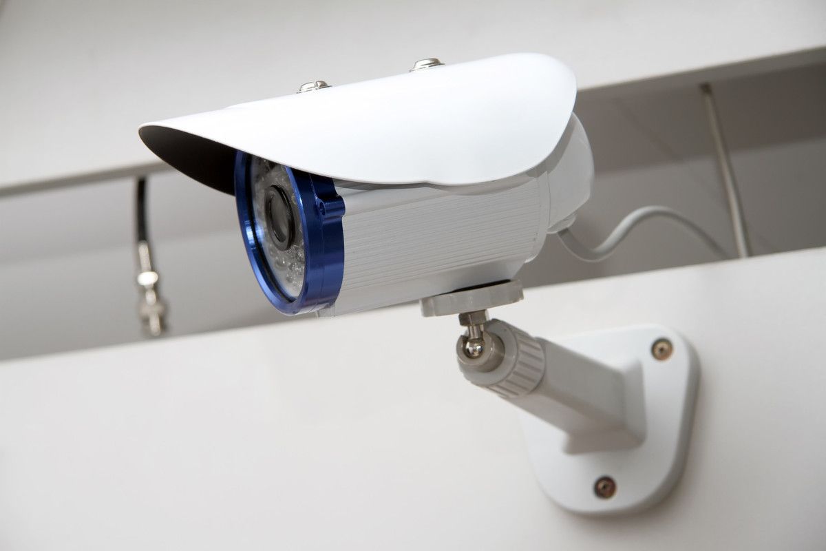 Caméra de sécurité blanche fixée au mur, orientée vers l'extérieur et dotée d'un cache-objectif bleu