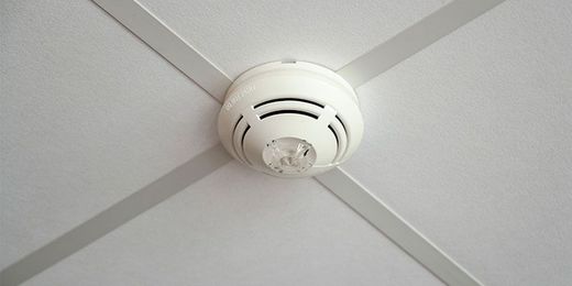 Détecteur de fumée blanc fixé au plafond avec des poutres entrecroisées