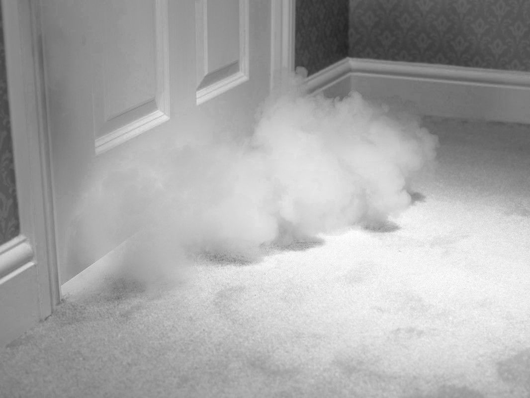 Nuage de fumée ou de vapeur s'échappant sous une porte fermée et tombant sur un sol recouvert de moquette