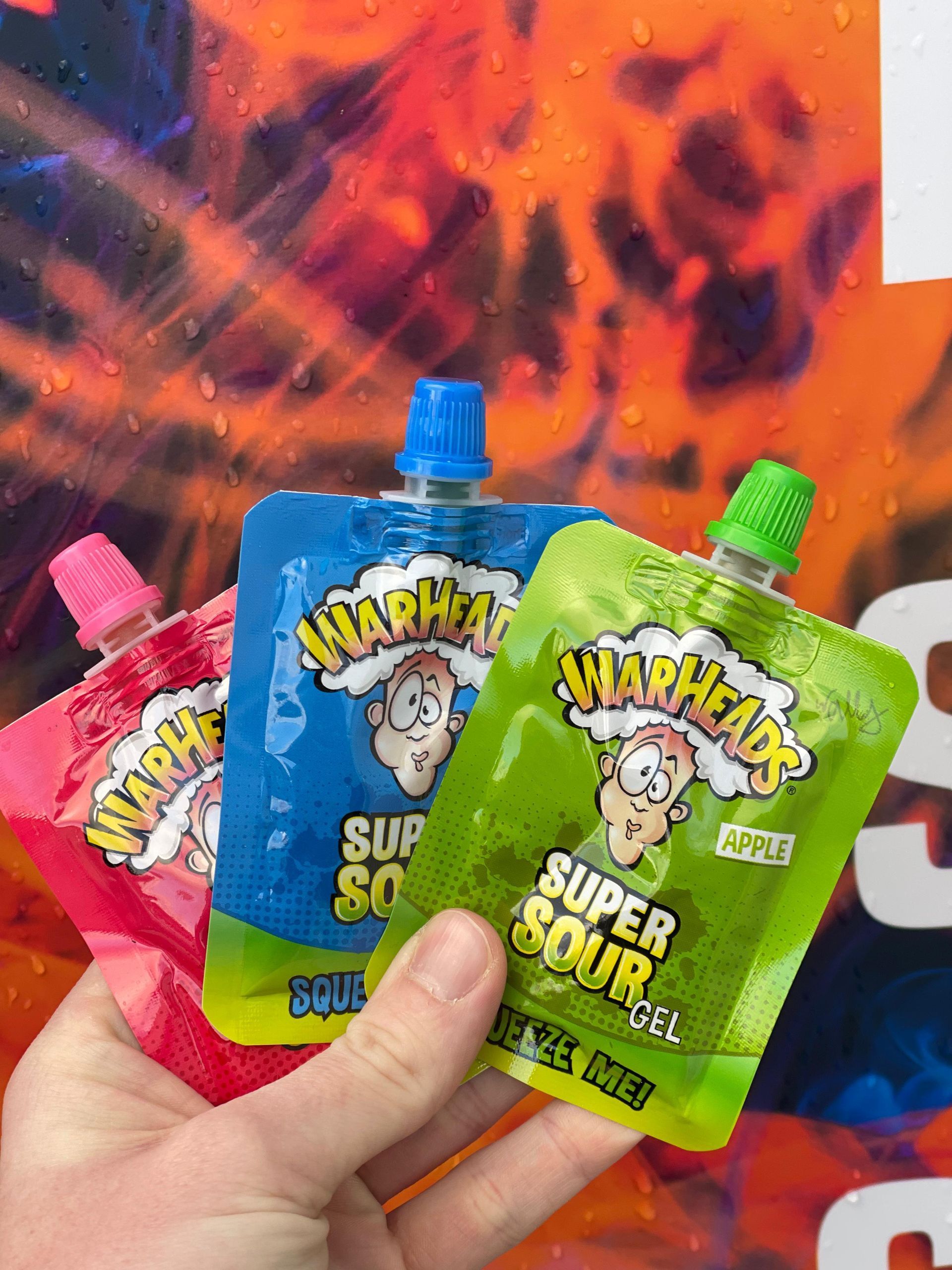Eine Person hält drei Beutel Warheads Super Sour Gel in der Hand.