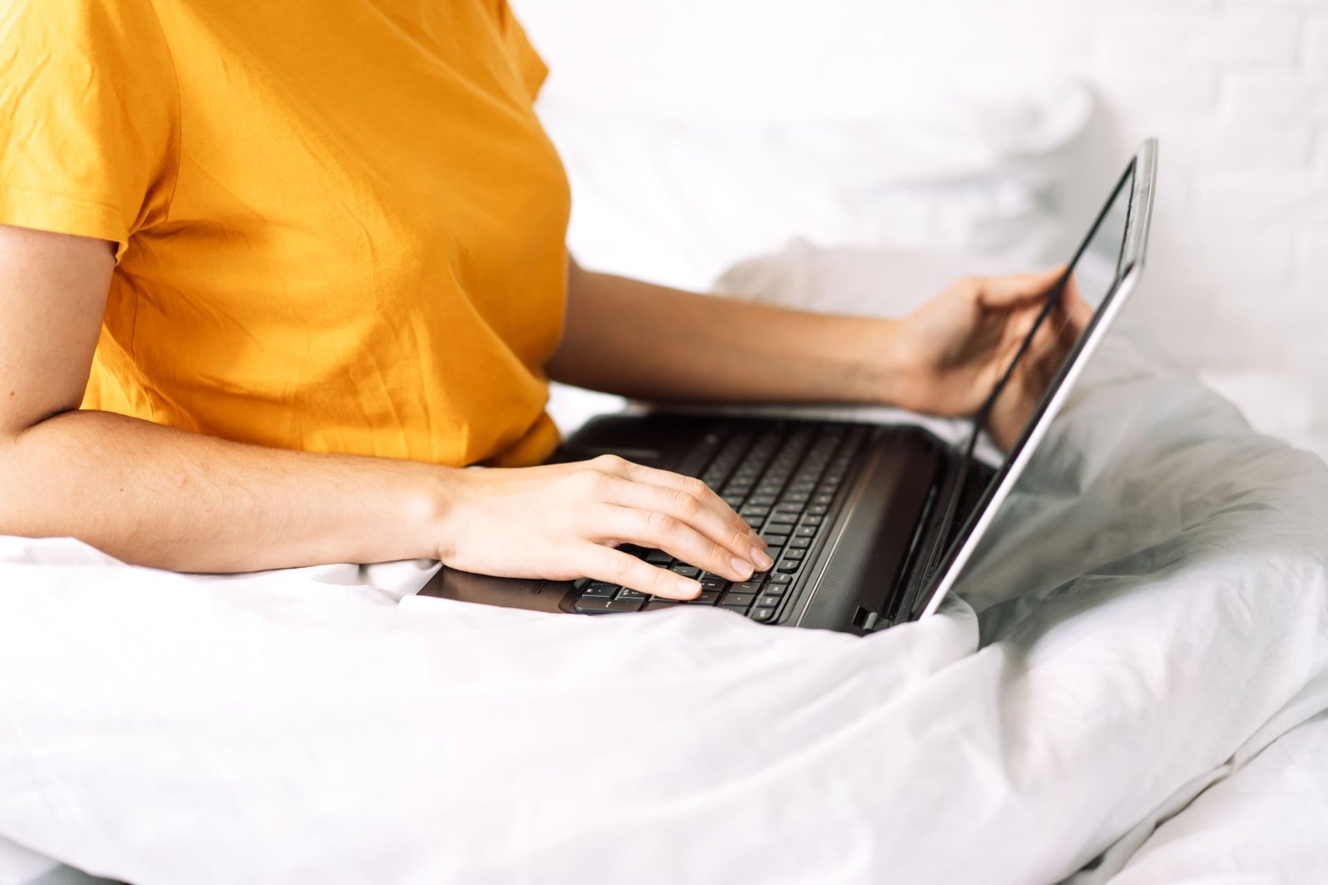 Una mujer está sentada en una cama usando una computadora portátil.