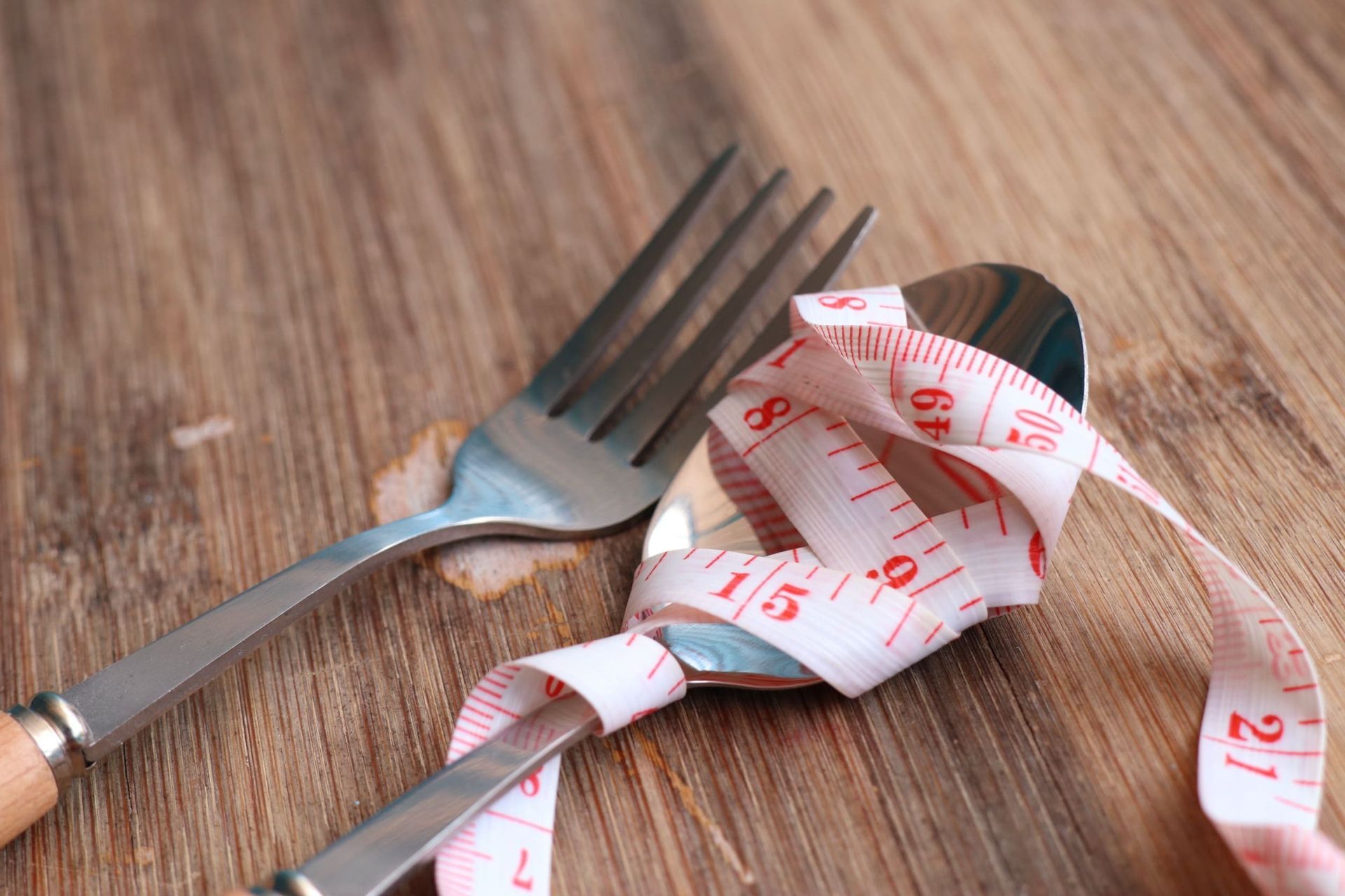 Una cinta métrica se enrolla alrededor de un tenedor y una cuchara sobre una mesa de madera.