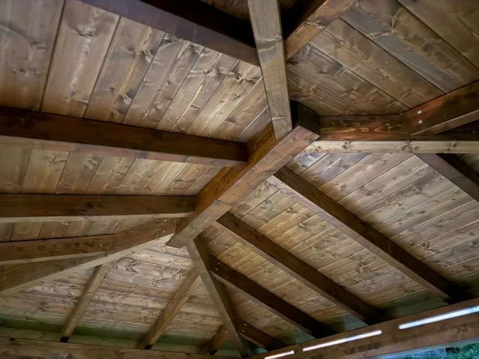 Techo de cenador de madera con vigas y tablones, teñido en tonos marrones cálidos.