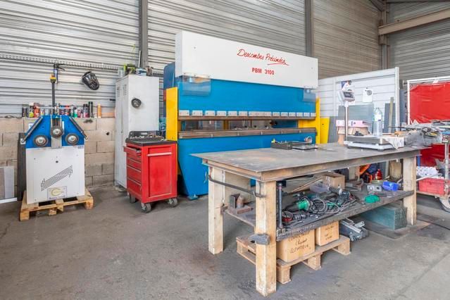 Atelier équipé pour le travail des métaux, comprenant une grande presse plieuse bleue et un établi.