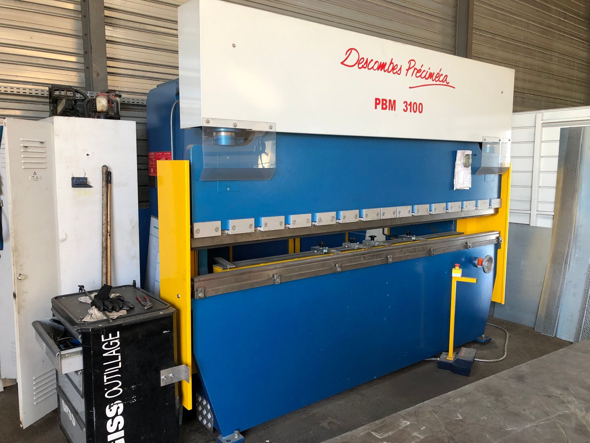 Presse plieuse à métaux bleue et jaune, dans un atelier.