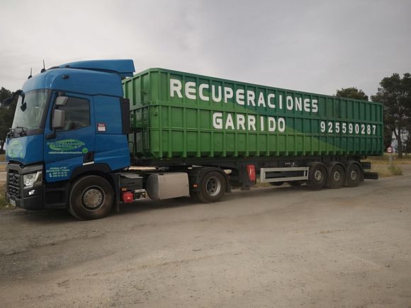Un camión tractor azul arrastrando un gran remolque de basura verde
