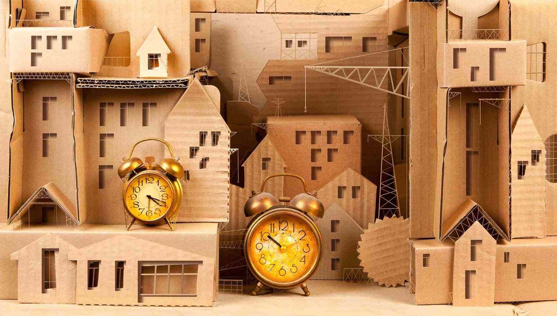 Dos relojes despertadores dorados se encuentran frente a una maqueta de cartón de una ciudad con edificios y torres.