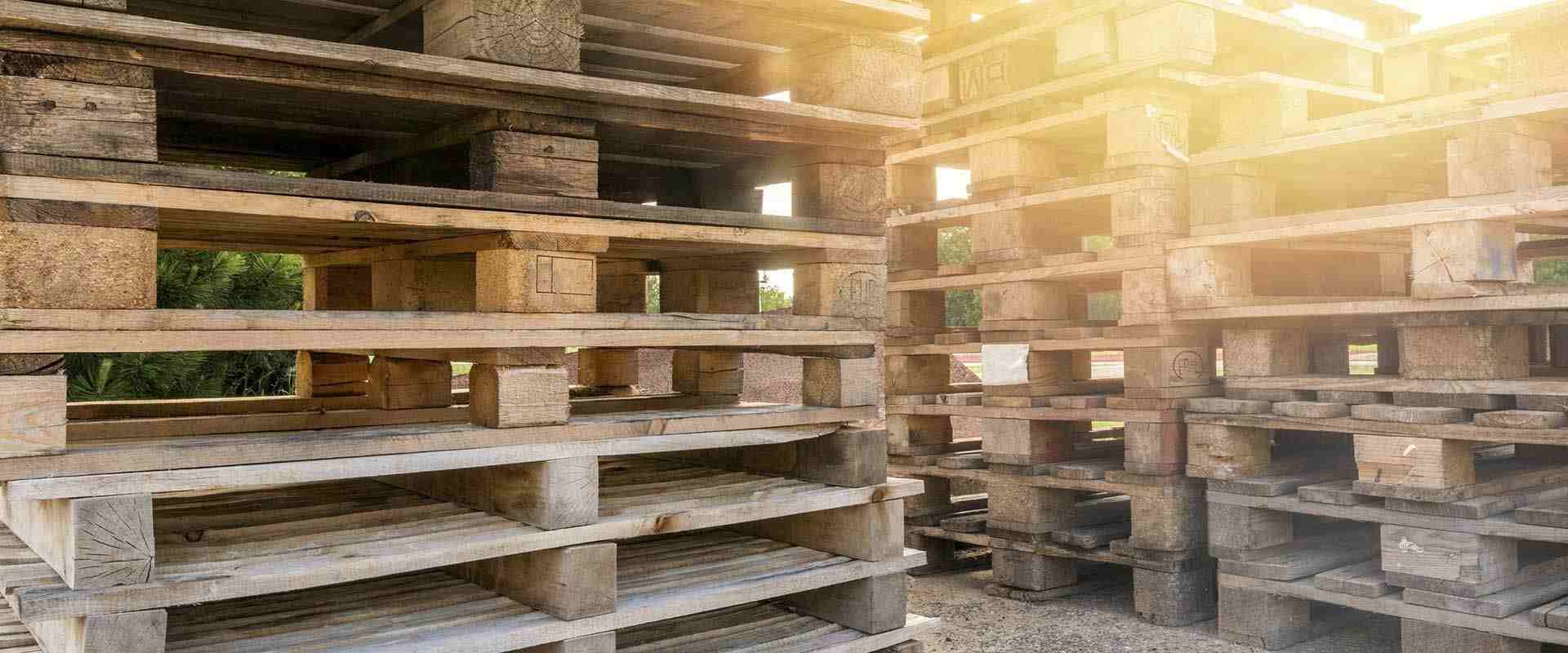 Dos pilas de palés de madera desgastados por el tiempo, apilados al aire libre bajo la luz cálida y brillante del sol.