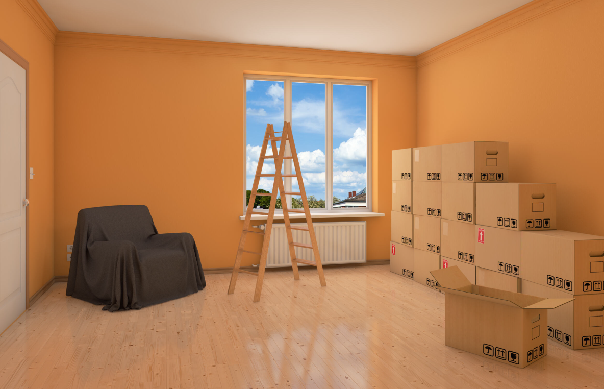 Habitación vacía con paredes naranjas, cajas, una escalera y una silla cubierta.