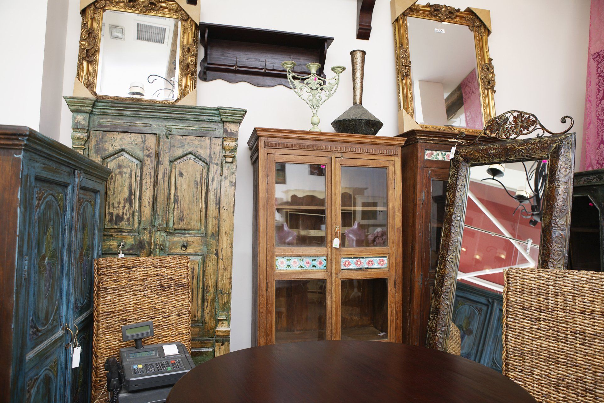 Una exposición de muebles: armarios antiguos, espejos y una mesa redonda en una tienda.