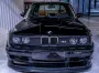 Vista frontal de un BMW E30 M3 clásico de color negro brillante en una sala de exposición interior limpia y bien iluminada.