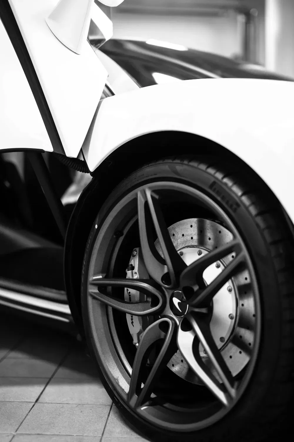 Primer plano en blanco y negro de la rueda delantera, la llanta de aleación y la puerta diédrica abierta de un coche.