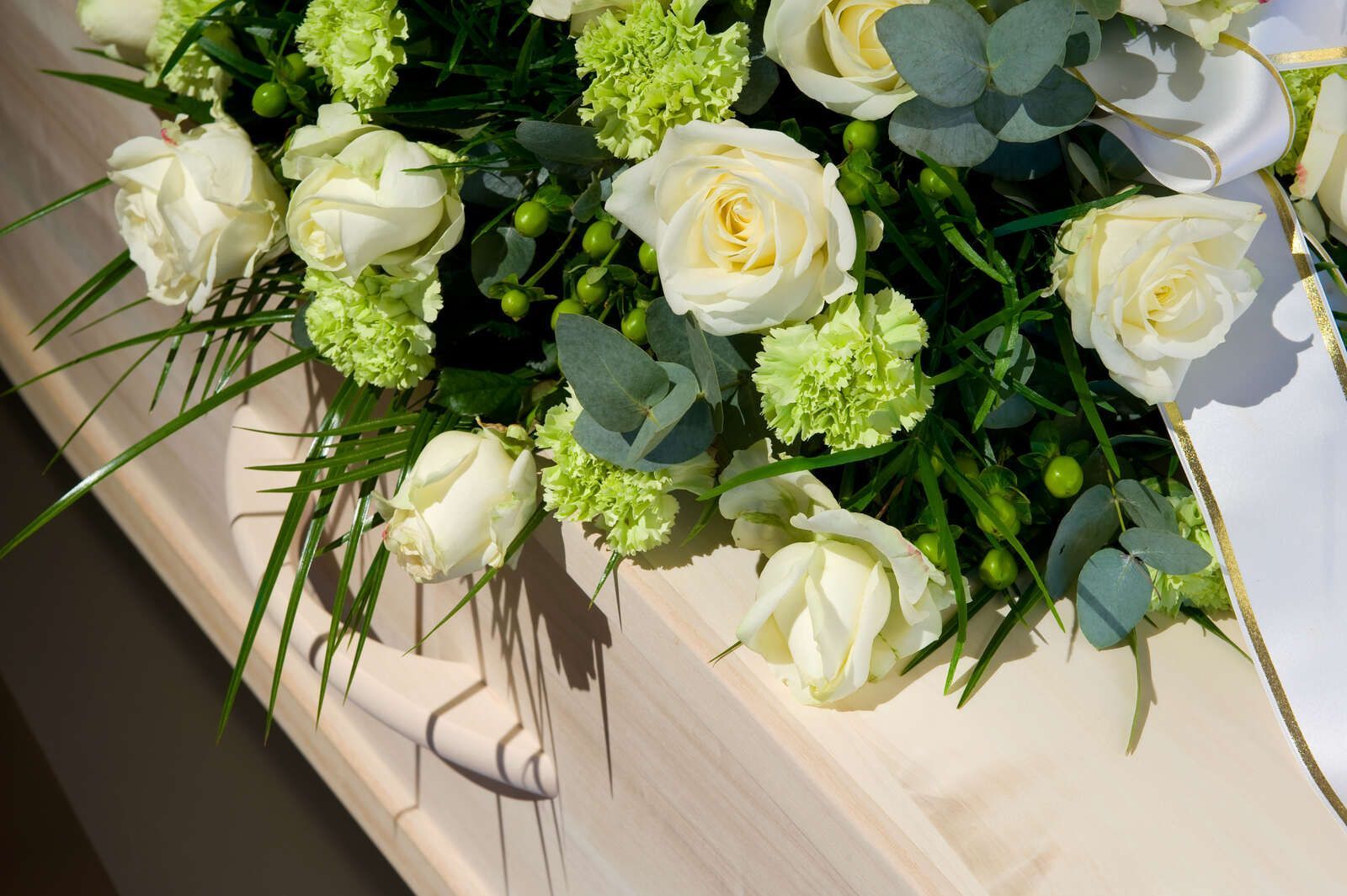 Ein Sarg mit weißen Rosen und grünen Nelken darauf.