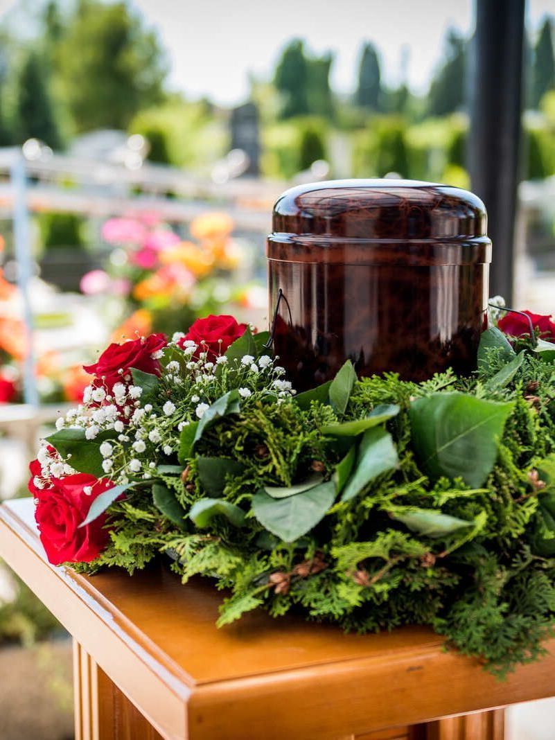 Ein Holztisch mit einer Urne und Blumen darauf.