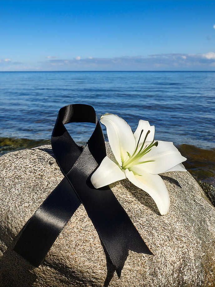 Ein schwarzes Band und eine weiße Blume auf einem Felsen in der Nähe des Ozeans