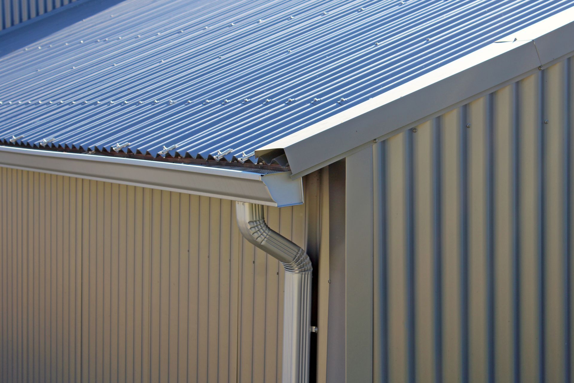 Toiture et bardage métalliques d'un bâtiment avec gouttière et descente pluviale.