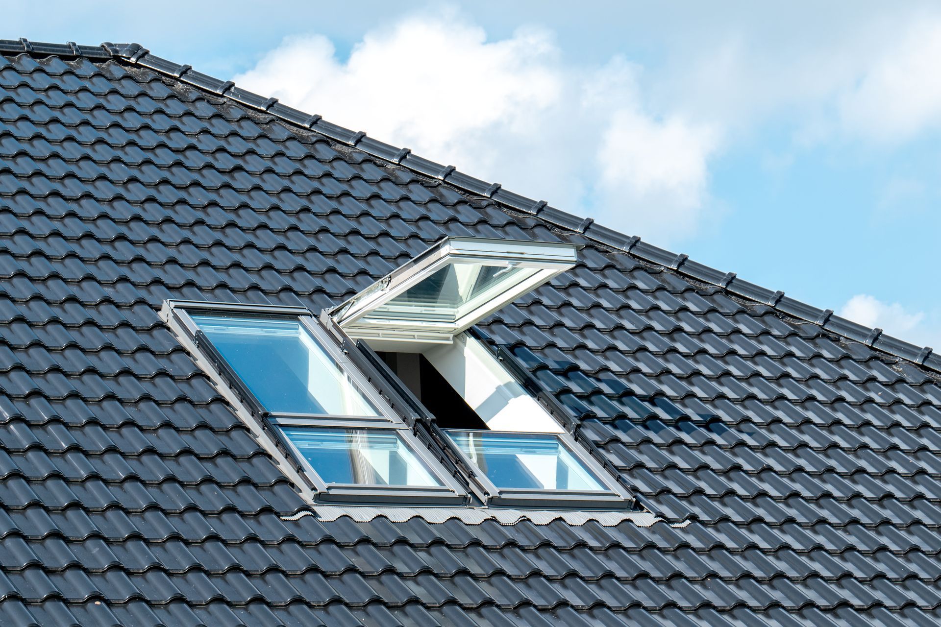 Des puits de lumière sur un toit de tuiles, dont un ouvert.