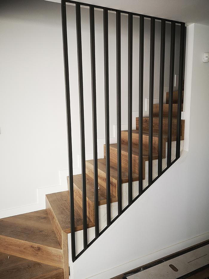 Escalera de madera con barandillas de metal negro contra una pared blanca.