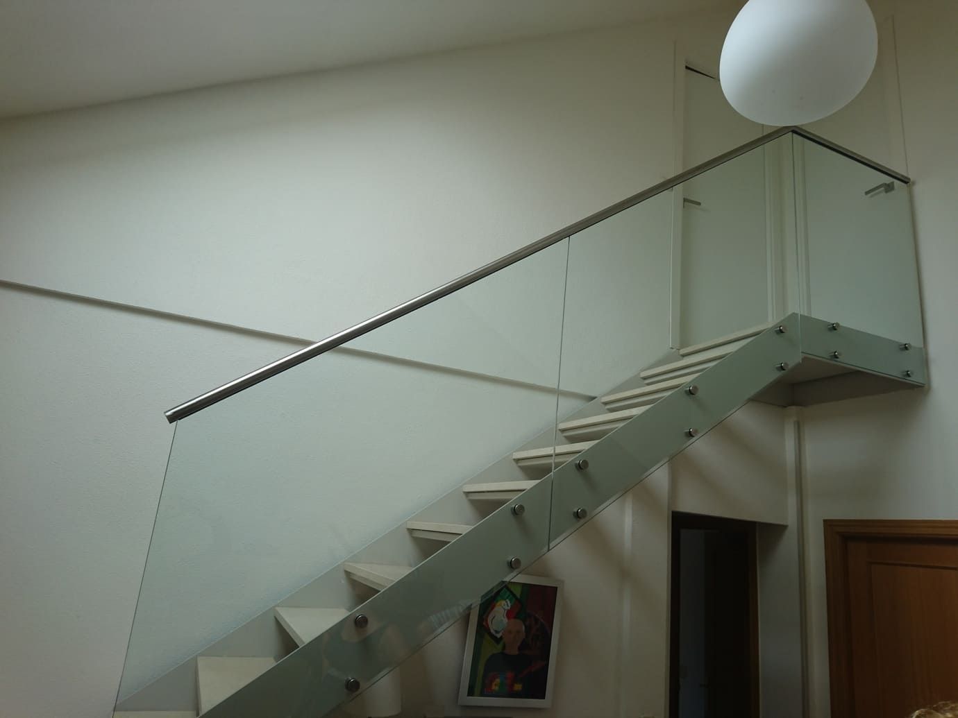 Escalera moderna con barandilla de cristal. Paredes y escaleras blancas. Se ve un cuadro.