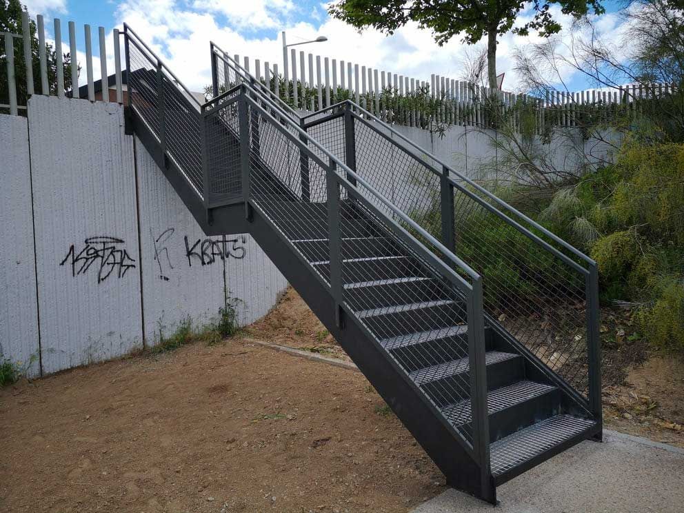 Escalera metálica con pasamanos junto a un muro de hormigón con grafitis.