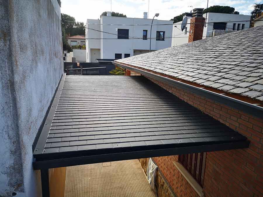 Un patio cubierto de color oscuro con techo texturizado, al lado de un edificio de ladrillo.