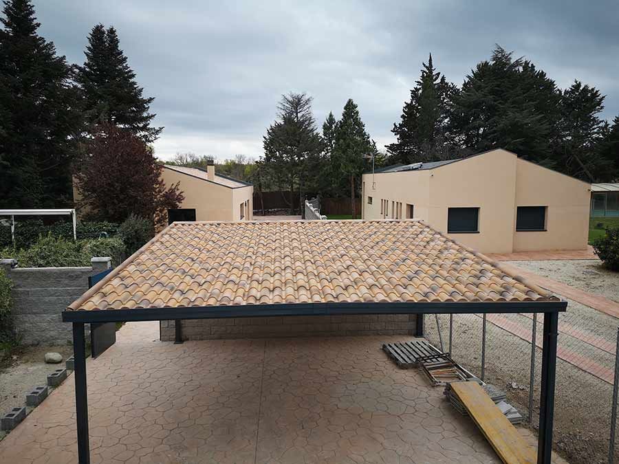 Cochera con techo de tejas, edificios de color beige y árboles bajo un cielo nublado.