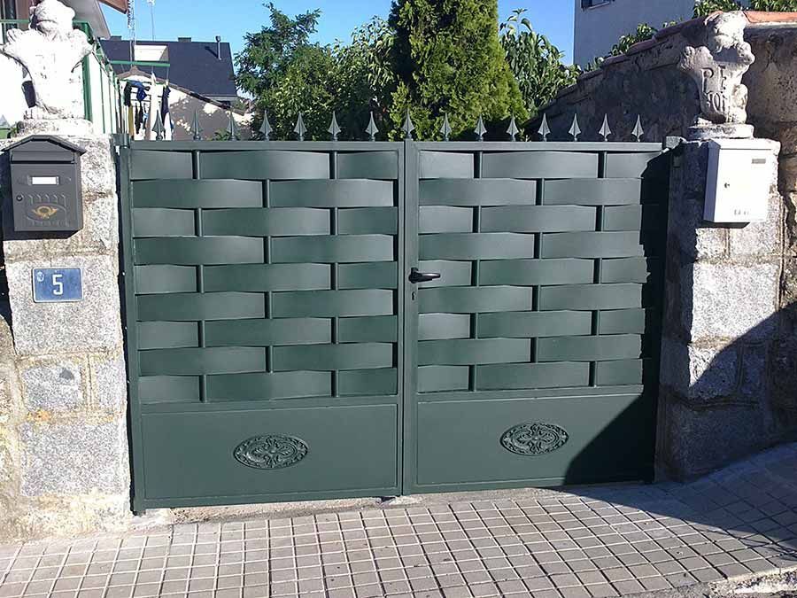 Puerta de metal verde con diseño tejido, pilares de piedra, buzón y número de dirección 5.
