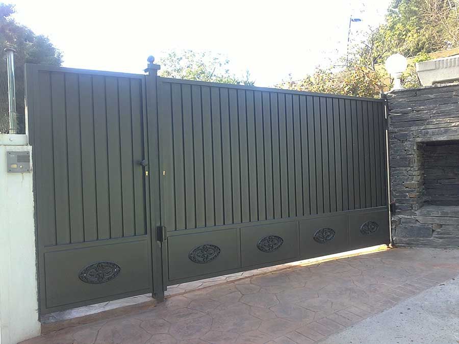 Puerta metálica de color verde con barrotes verticales y óvalos decorativos.