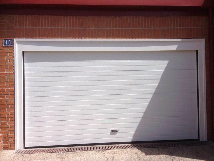 Puerta de garaje blanca con líneas horizontales, contra pared de ladrillo, con luz natural.