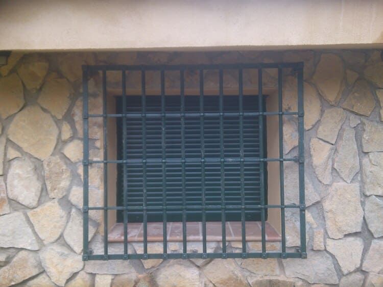 Ventana con rejas y contraventanas de metal verde en pared de piedra.