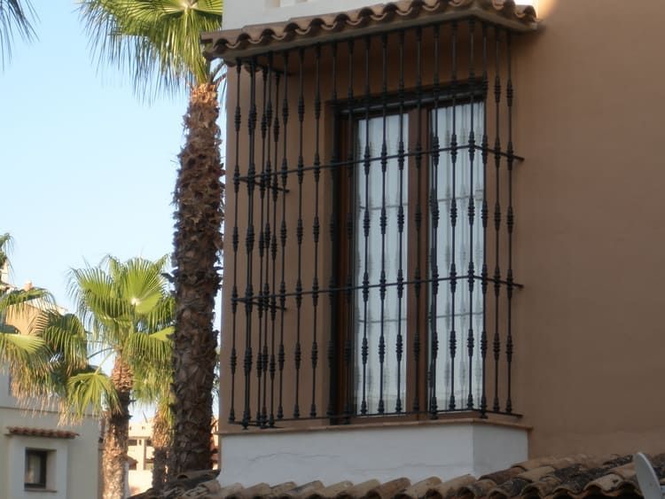 Ventana con rejas de hierro forjado negro, edificio color canela, palmera al frente.