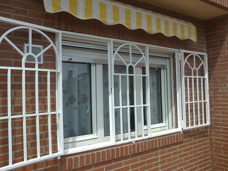 Ventana con barrotes blancos y toldo de rayas amarillas en un edificio de ladrillo.
