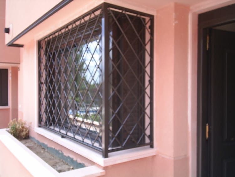 Barras de seguridad marrones en una ventana ubicada en un exterior de edificio de color rosa pálido.