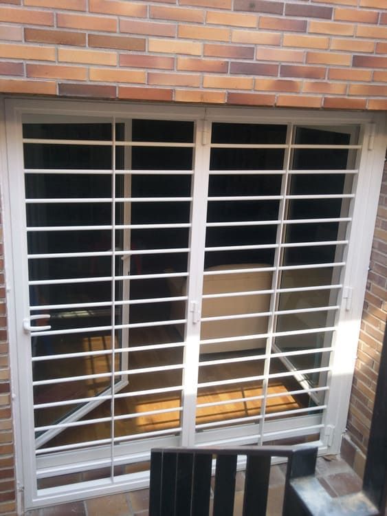 Puerta corrediza de vidrio con barrotes blancos contra una pared de ladrillos.