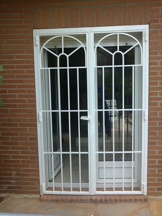 Puerta de seguridad blanca con parte superior arqueada y rejas en un edificio de ladrillo.