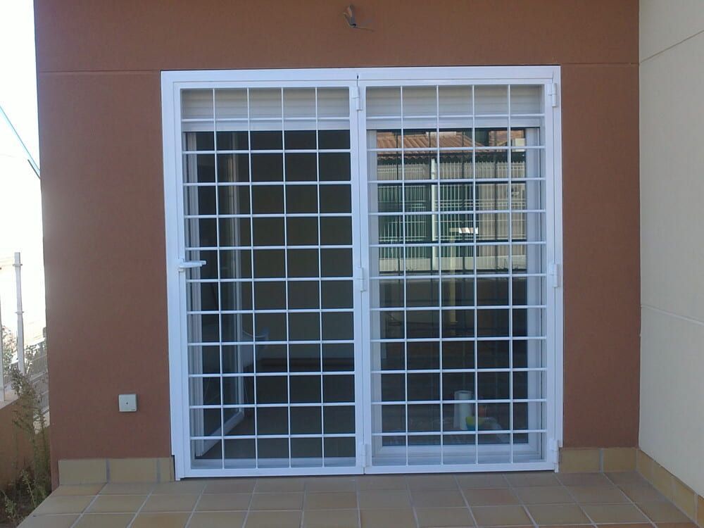 Rejas de seguridad blancas sobre puertas corredizas de vidrio en un edificio marrón.