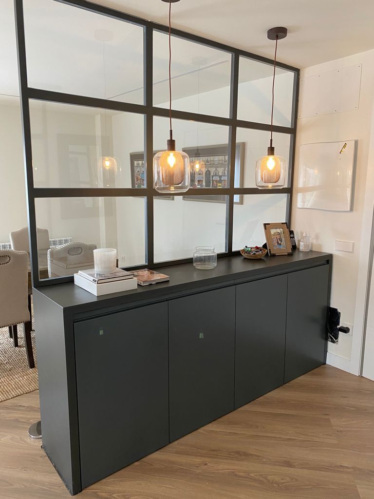 Mueble gris oscuro con separador de ambientes de cristal y metal negro, lámparas colgantes.
