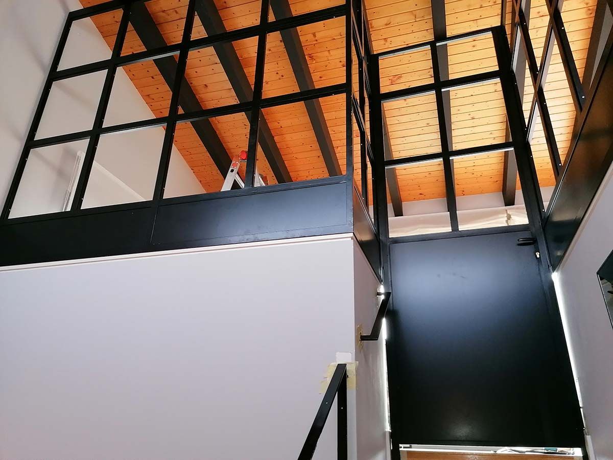 Barandilla y escalera de metal negro en un edificio con paredes blancas y techo de madera.