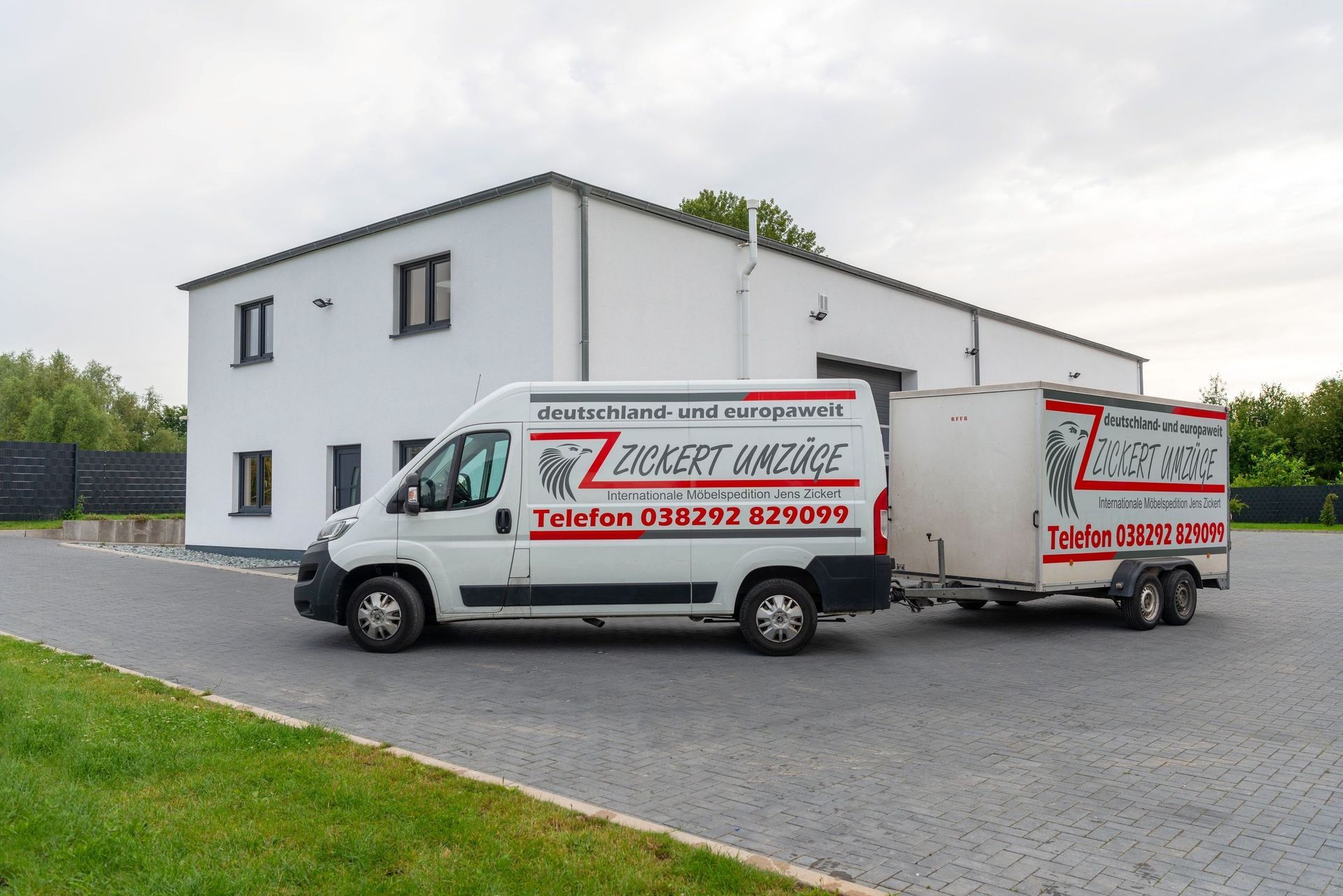 Weißer Lieferwagen und Anhänger mit Firmenlogo vor einem weißen Gebäude geparkt.