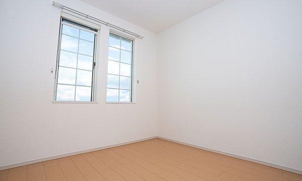 Leerer Raum mit zwei Fenstern, weißen Wänden und hellem Holzboden.