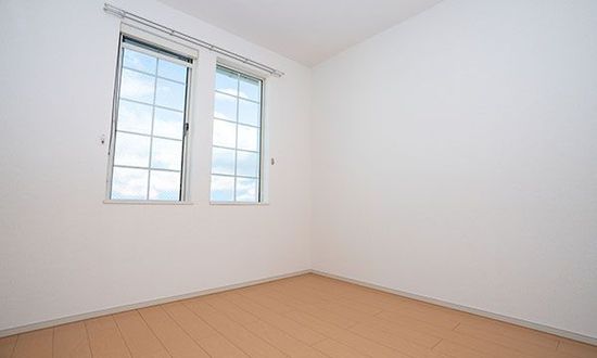 Leerer Raum mit zwei Fenstern, weißen Wänden und hellem Holzboden.
