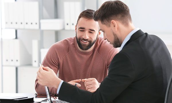 Zwei Männer in einem Büro, einer im Anzug, der andere im Pullover, untersuchen etwas aufmerksam.