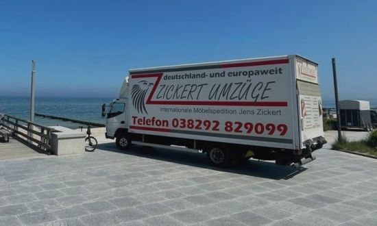 Umzugswagen parkt auf einem Pier mit Meerblick, strahlend blauer Himmel. ZICKERT UMZÜGE an der Seite des LKWs.