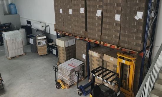 Lagerinnenraum mit auf Regalen gestapelten Kisten, einem Palettenwagen und anderer Ausrüstung.