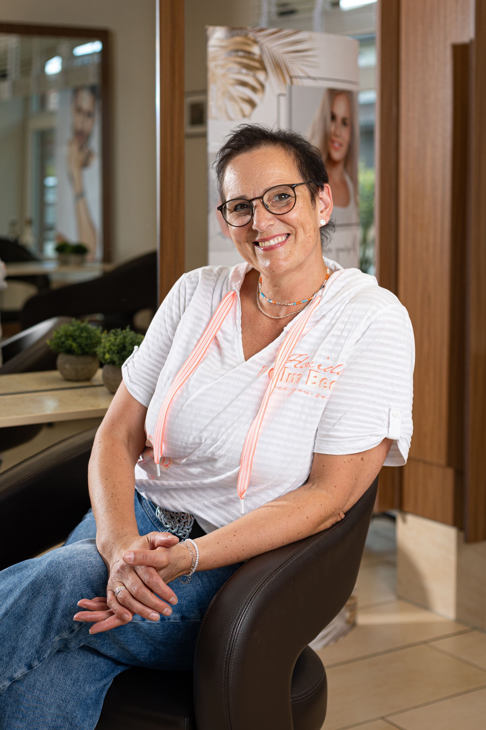 Eine Frau sitzt in einem Salon auf einem Stuhl und lächelt.